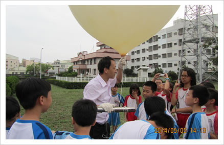 學童參與環境教育活動的照片，畫面中講師正拿著高空探測氣球，向學童進行施放說明。