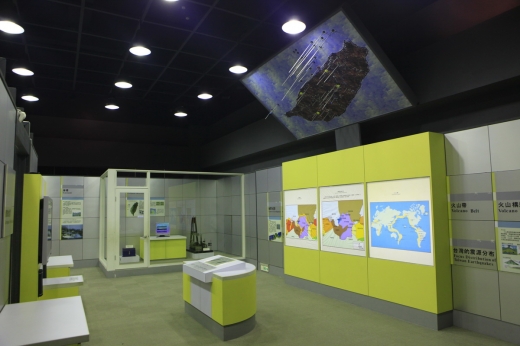 這是一張從右方側身的角度來看臺灣地震分布展區的圖，除了上方的互動螢幕外，牆面上也有三張圖片說明世界各地地震帶的分布介紹。